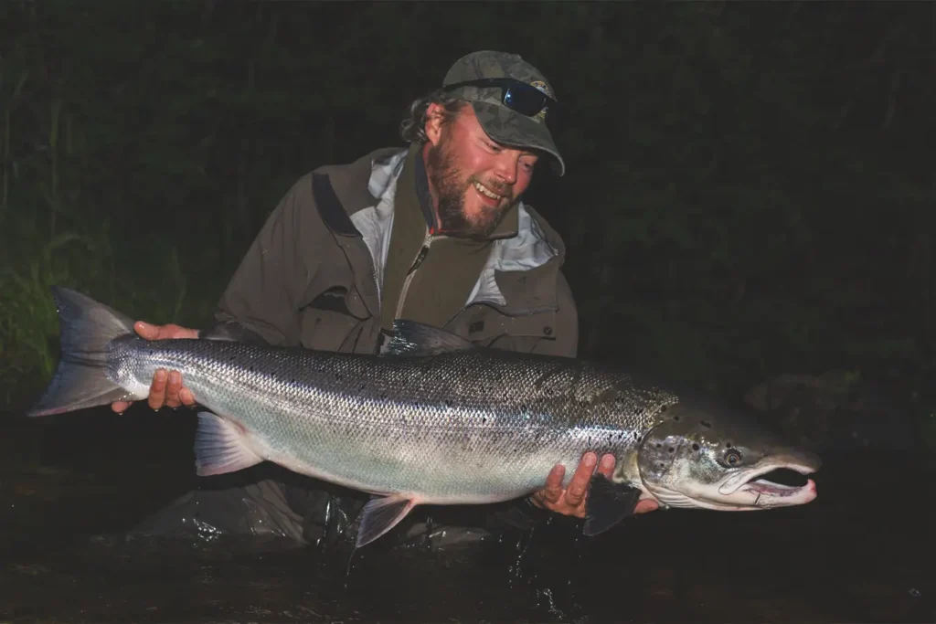 A man showcasing exceptional Gaula fishing skills while holding a large salmon in the water.