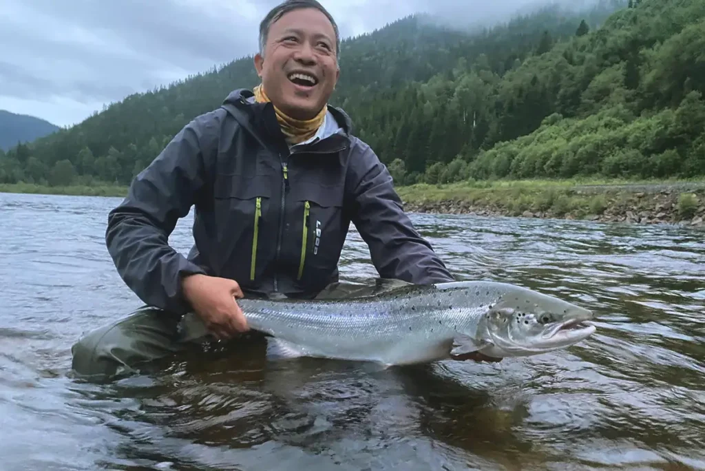 En mann som viser frem en fisk i en elv.