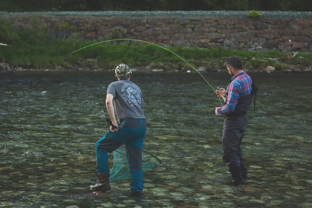 To menn nyter Gaulafiske der de står i en elv med fluestang.