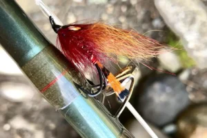 A fly fishing rod with a red and orange fly attached to it.
