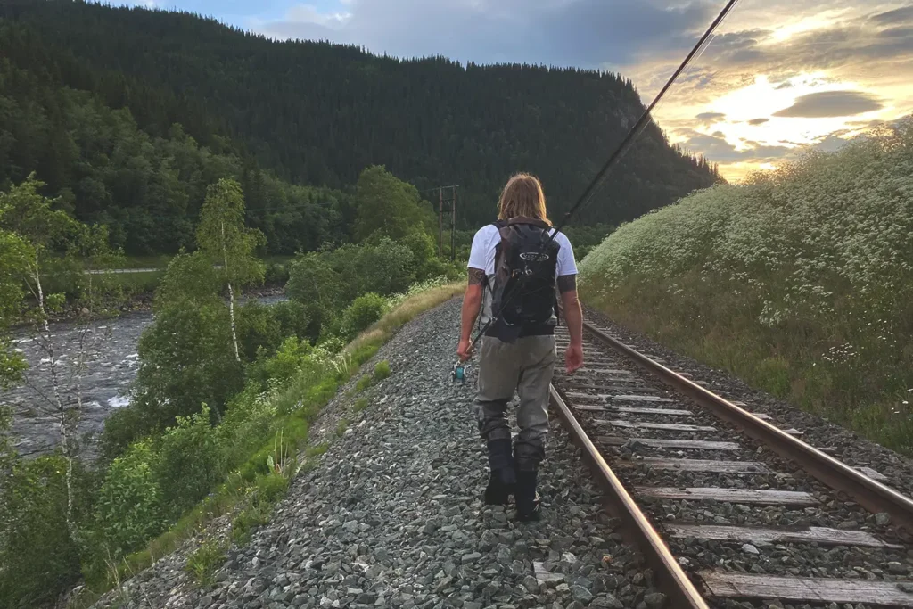 A man walking on a train track near a river gathers information.