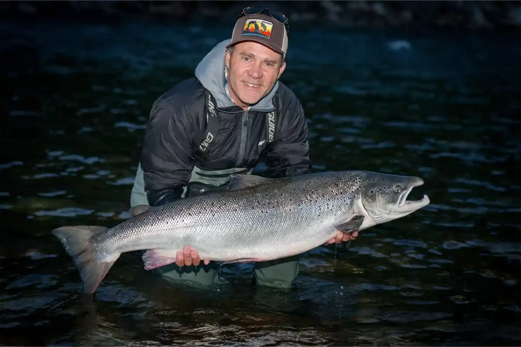 A man holding a large salmon in the water.