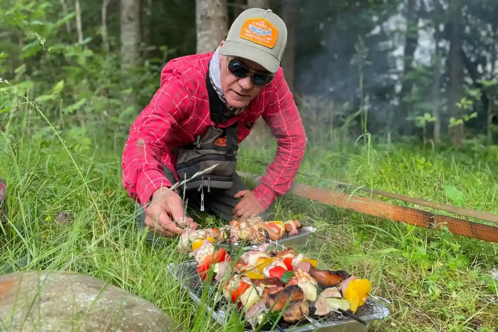 A man preparing food on a grill in the woods.
