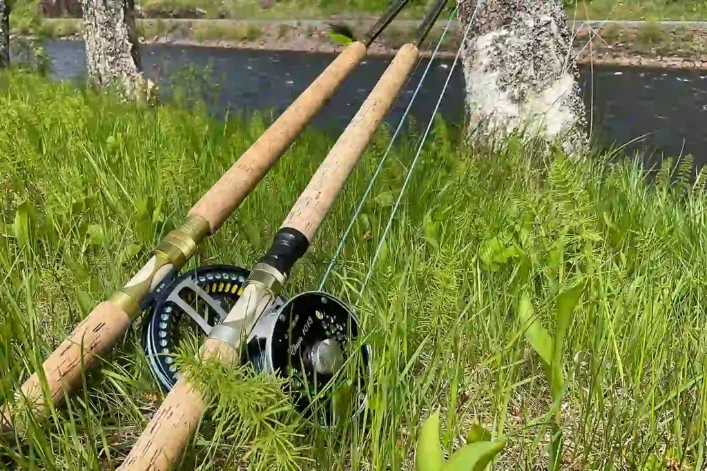 A fly rod and reel sitting in the grass next to a river.