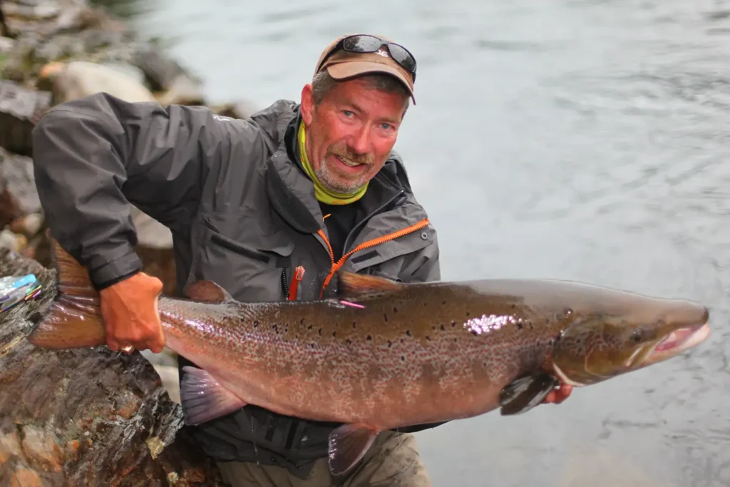 A man holding up a large fish in a river.