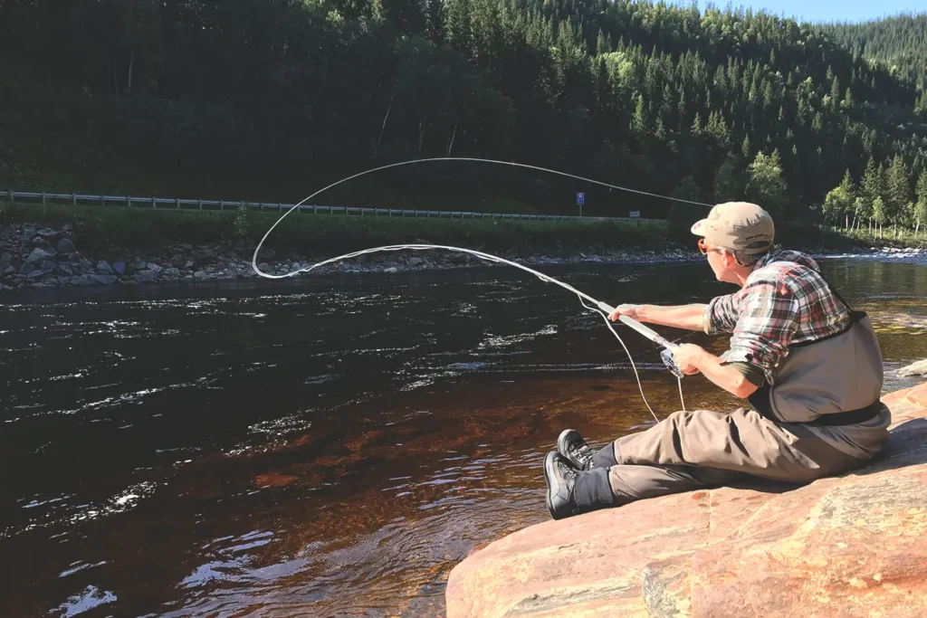 A man is enjoying relaxation by sitting on a rock and fishing in the Gaula river.