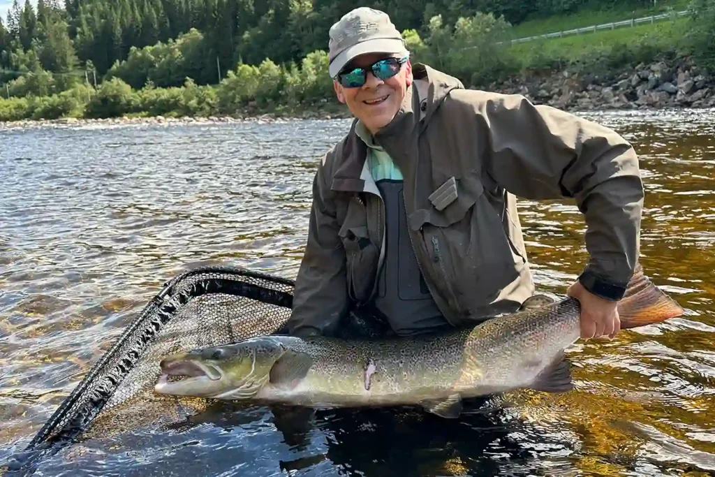 Man posing with a large fish caught in a river.