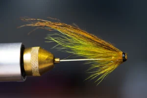 Close-up of a hand-tied fly fishing lure in a clamp with golden fibers.