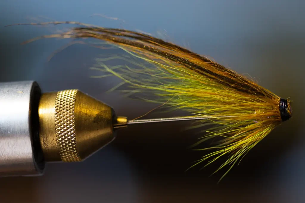 A close-up of a handmade fly fishing lure clamped in a vise.